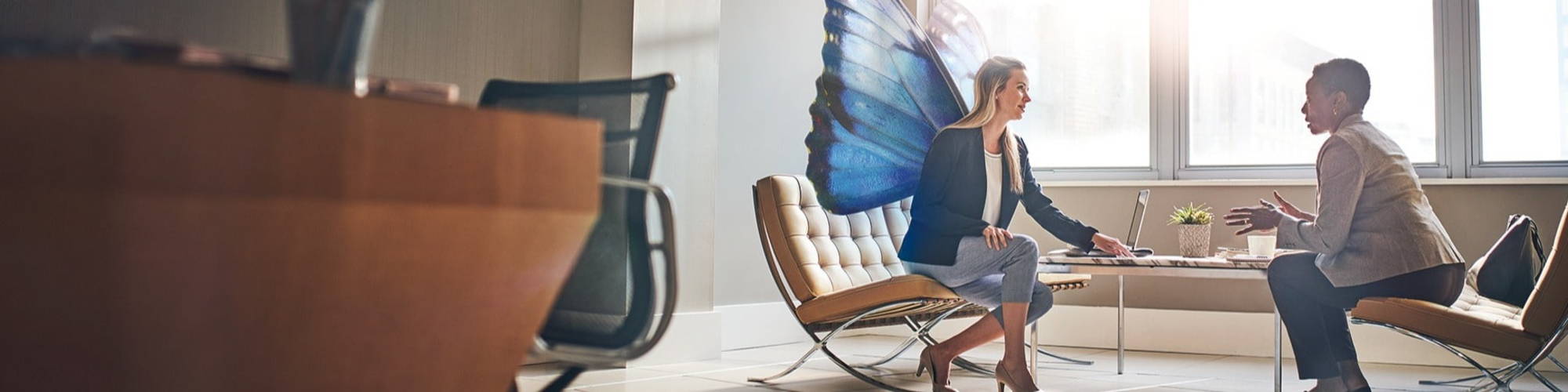 two women talking on office table, one with butterfly wings